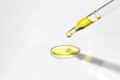 Photo of Cosmetic oil dripping from pipette on light grey background, closeup