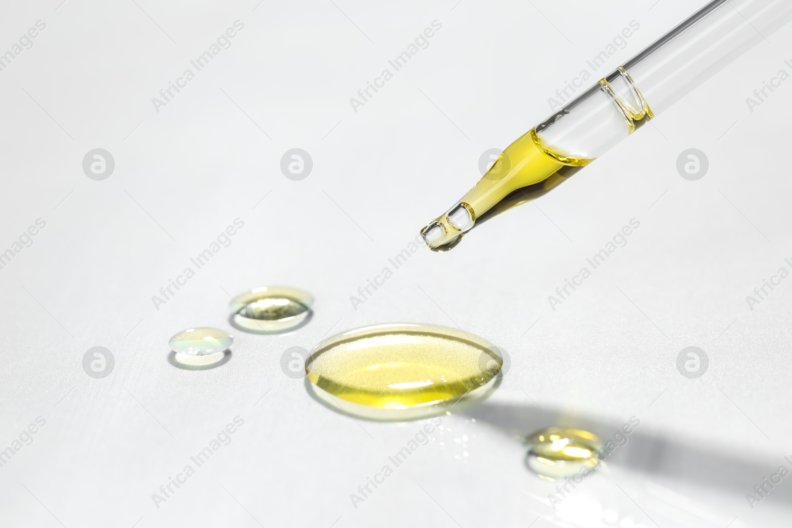 Photo of Cosmetic oil dripping from pipette on light grey background, closeup