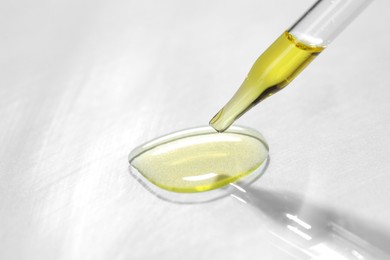 Photo of Cosmetic oil dripping from pipette on light grey background, closeup