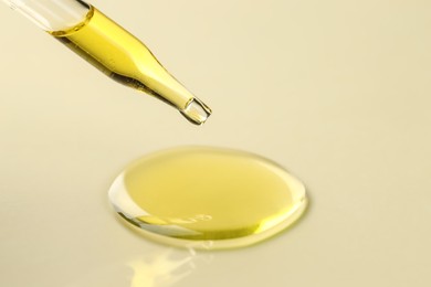 Cosmetic oil dripping from pipette on dark beige background, closeup. Space for text