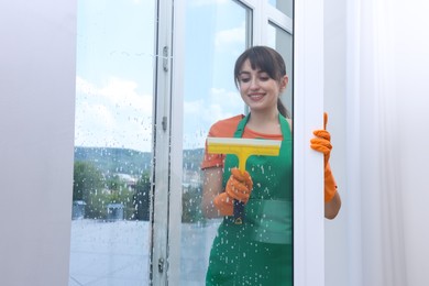 Young housewife with squeegee cleaning window indoors