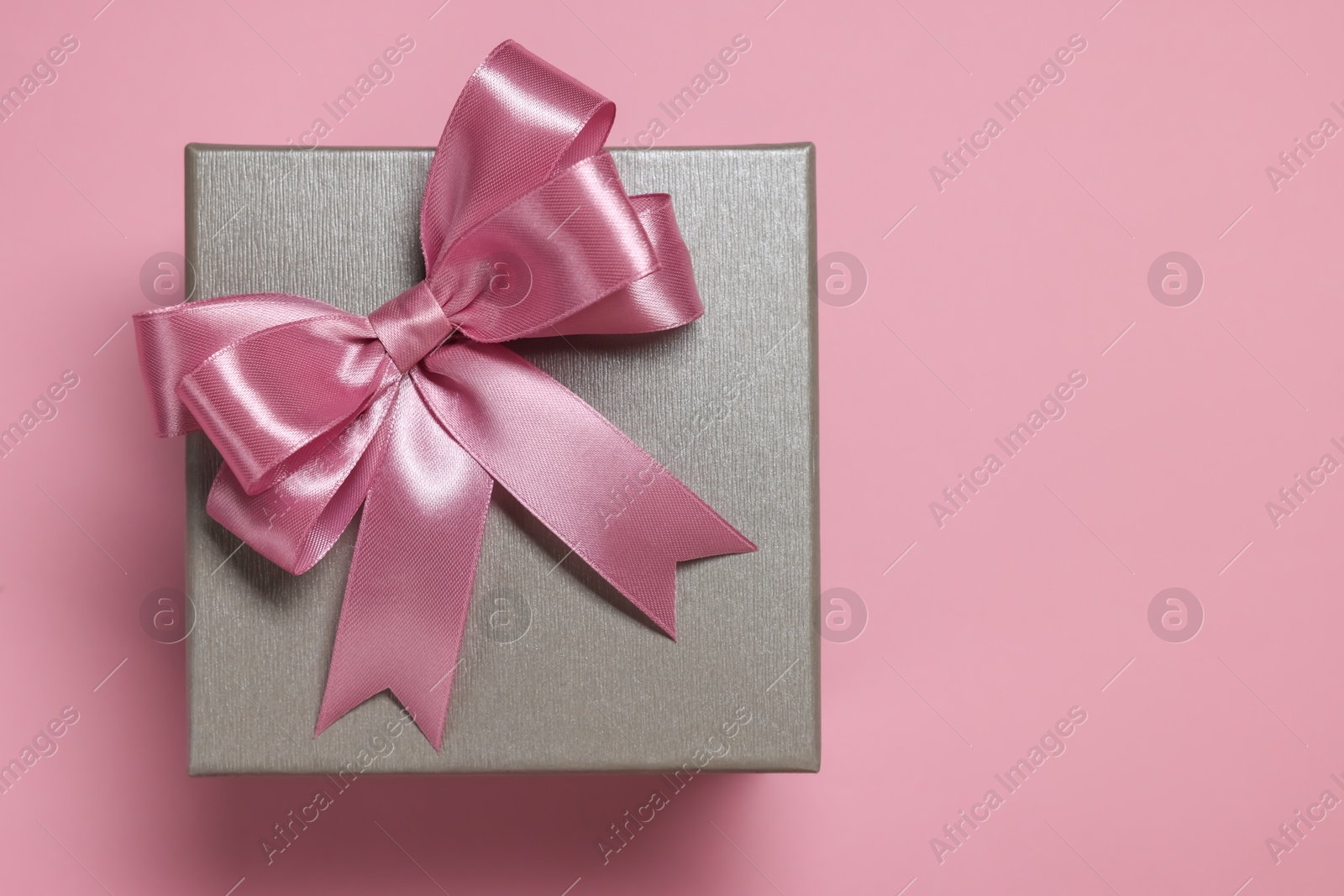 Photo of Gift box with bow on dusty pink background, top view. Space for text