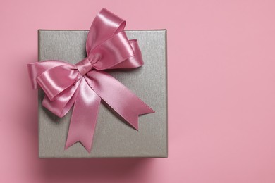 Gift box with bow on dusty pink background, top view. Space for text