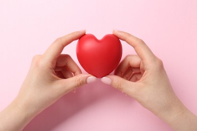 Photo of Woman holding red heart on pink background, top view