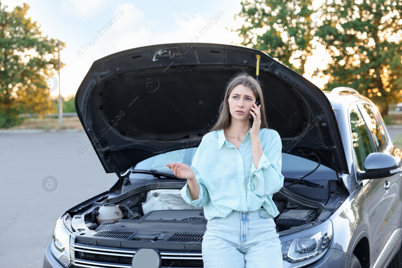 Photo of Stressed woman talking on phone near broken car outdoors