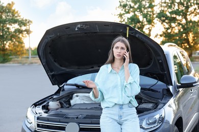 Stressed woman talking on phone near broken car outdoors