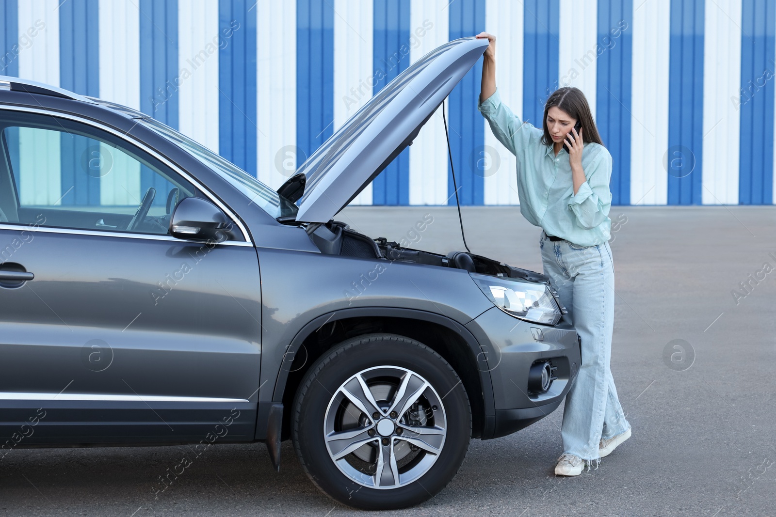 Photo of Stressed woman talking on phone near broken car outdoors