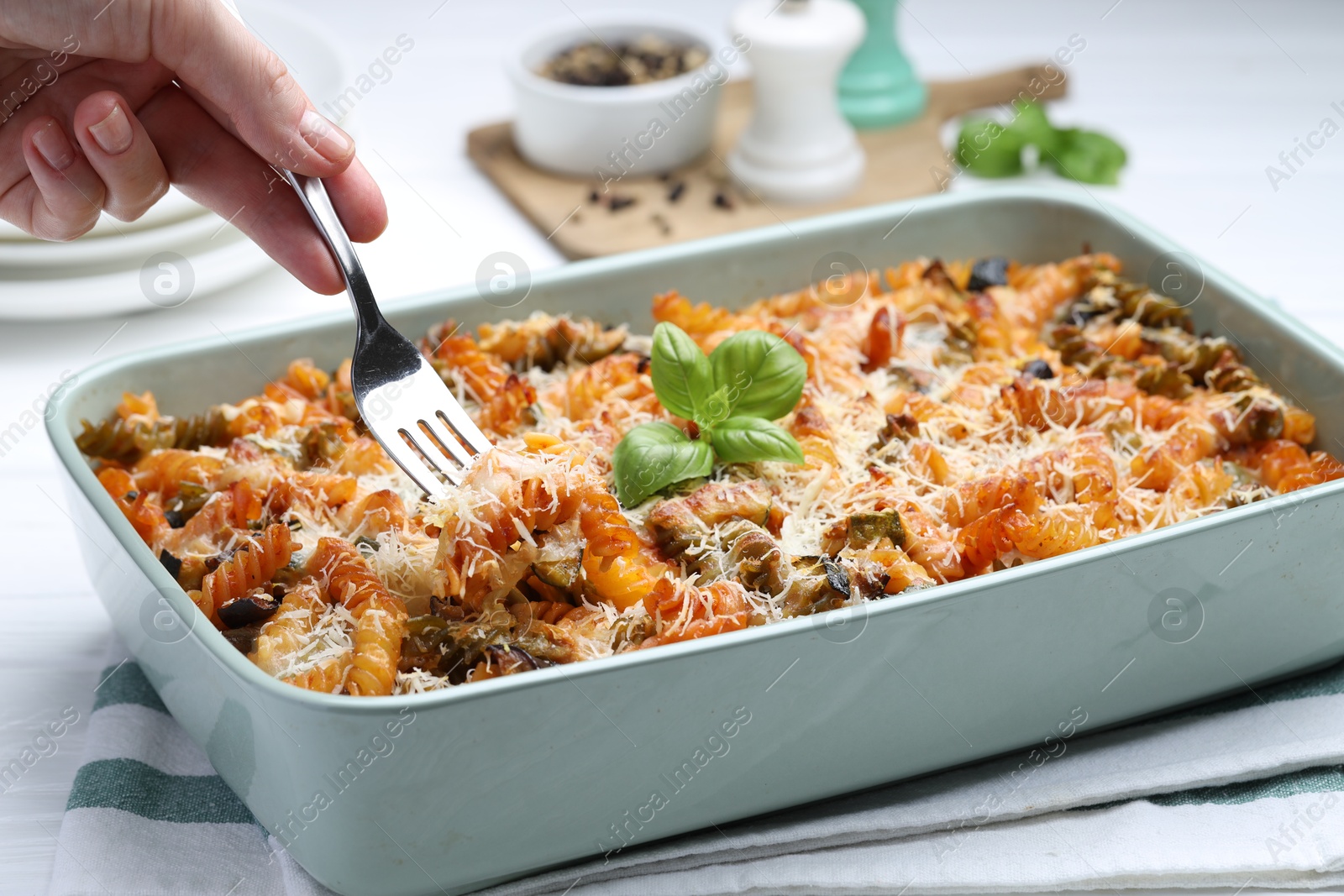 Photo of Woman eating delicious al forno pasta at white table, closeup