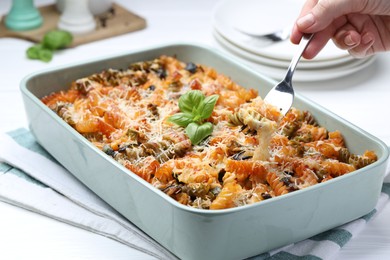 Photo of Woman eating delicious al forno pasta at white table, closeup