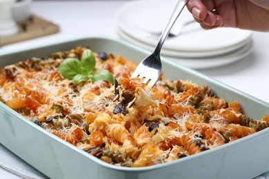 Photo of Woman eating delicious al forno pasta at white table, closeup