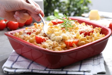 Photo of Woman eating delicious al forno pasta at grey table, closeup