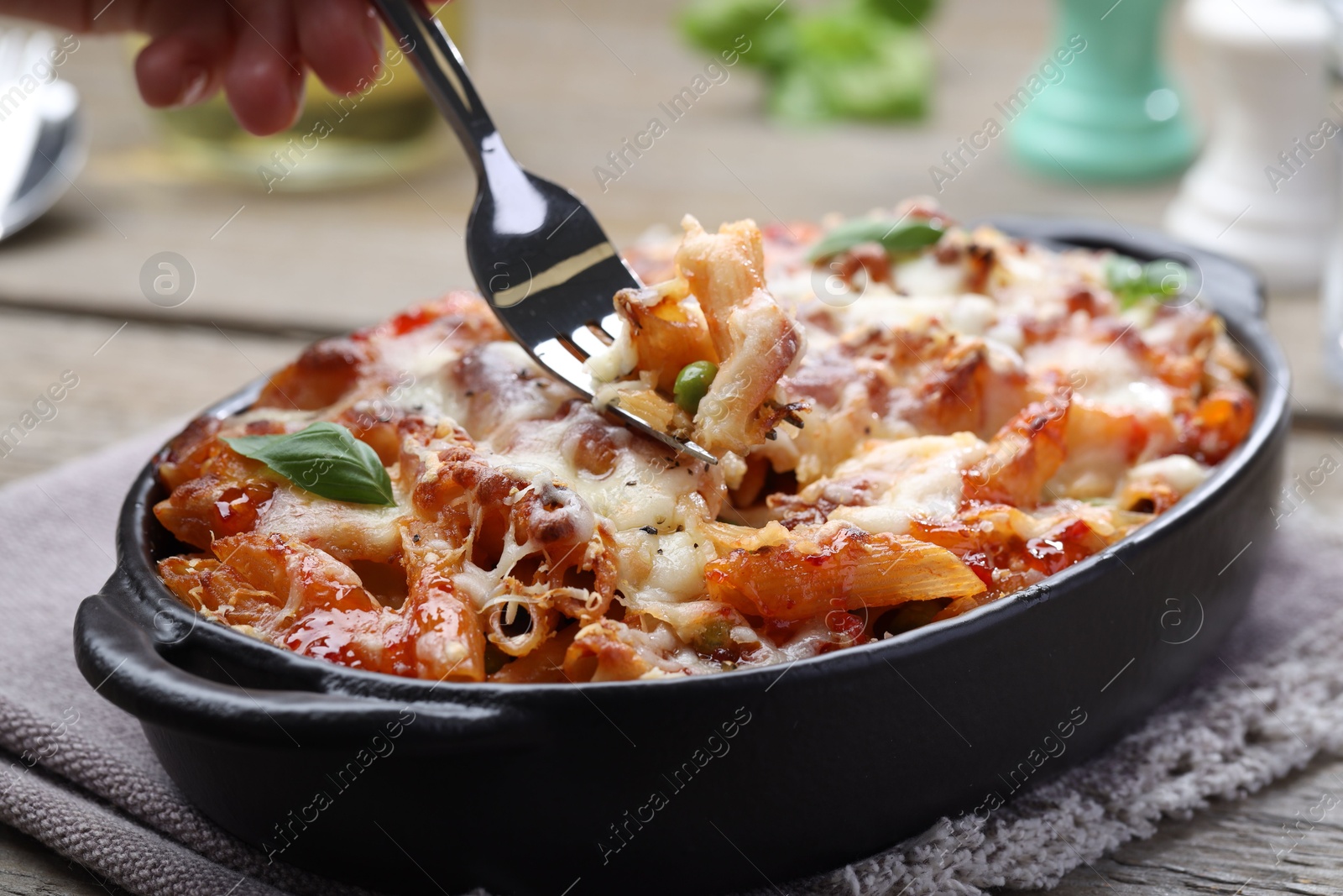 Photo of Woman eating delicious al forno pasta at wooden table, closeup