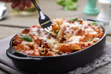 Photo of Woman eating delicious al forno pasta at wooden table, closeup