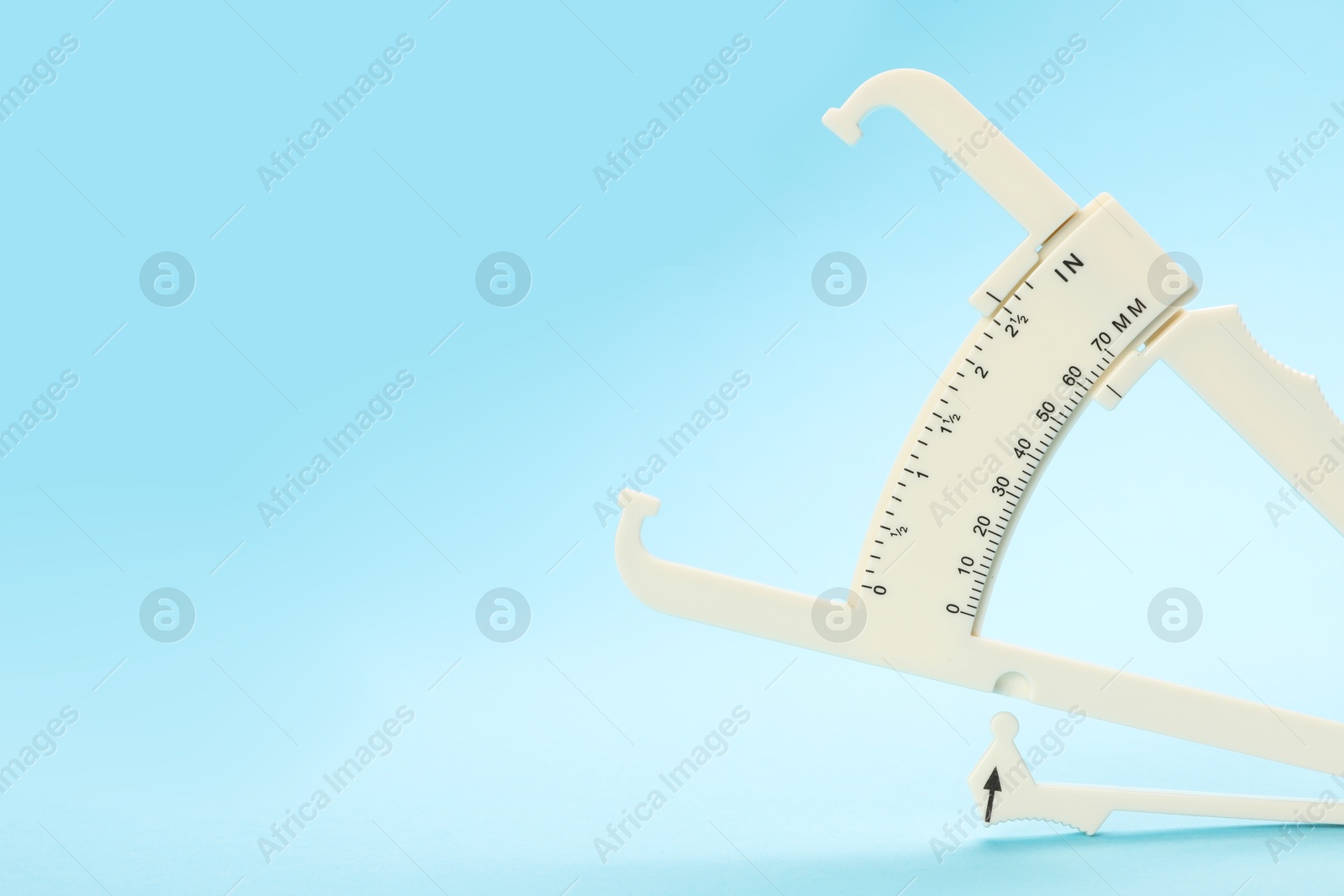 Photo of Plastic body fat caliper on light blue background. Space for text