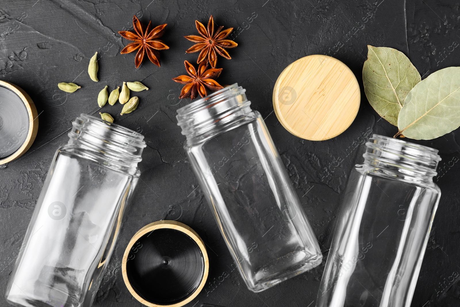 Photo of Different spices and glass jars on black table, flat lay