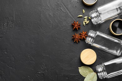 Photo of Different spices and glass jars on black table, flat lay. Space for text