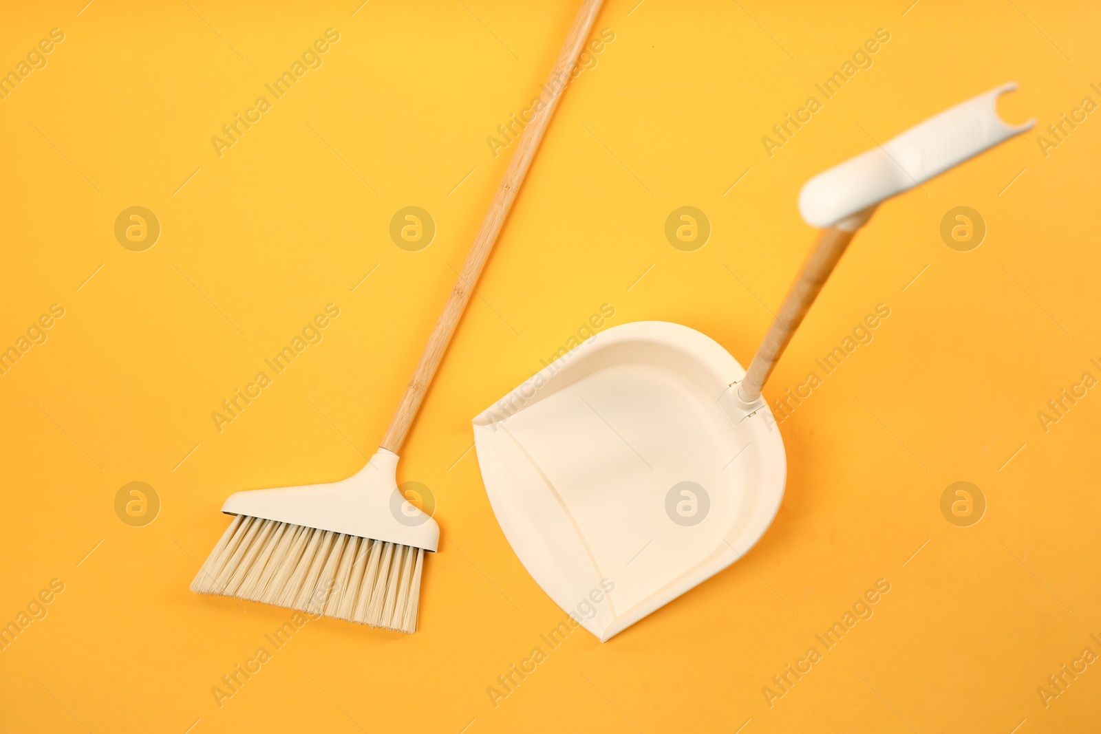 Photo of Cleaning broom and dustpan on orange background, flat lay