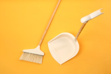 Cleaning broom and dustpan on orange background, flat lay