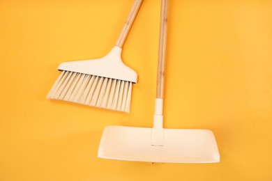 Photo of Cleaning broom and dustpan on orange background, flat lay