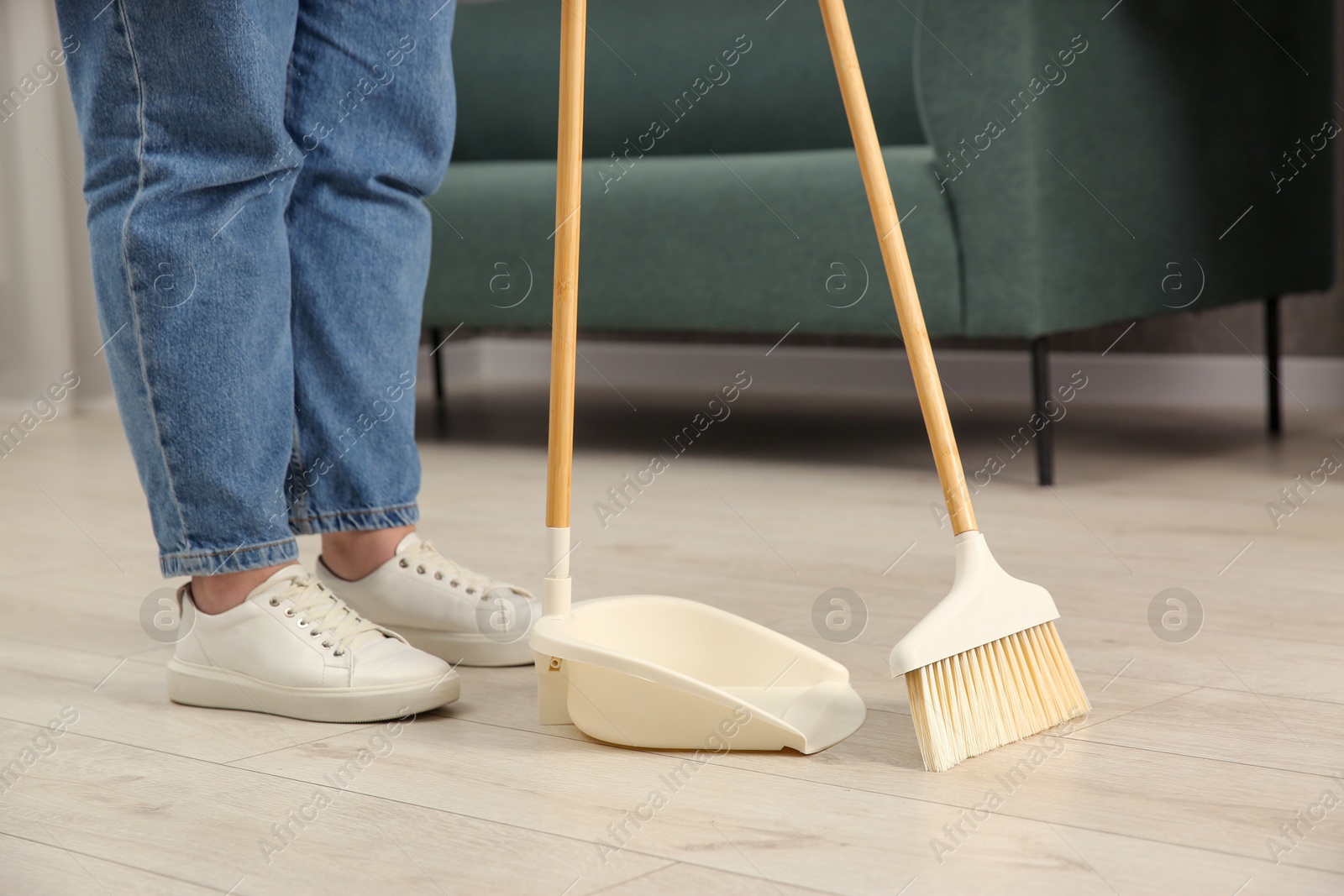 Photo of Woman with broom and dustpan cleaning floor indoors, closeup