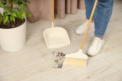 Photo of Woman with broom and dustpan cleaning floor indoors, closeup