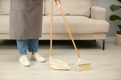 Photo of Woman with broom and dustpan cleaning floor indoors, closeup