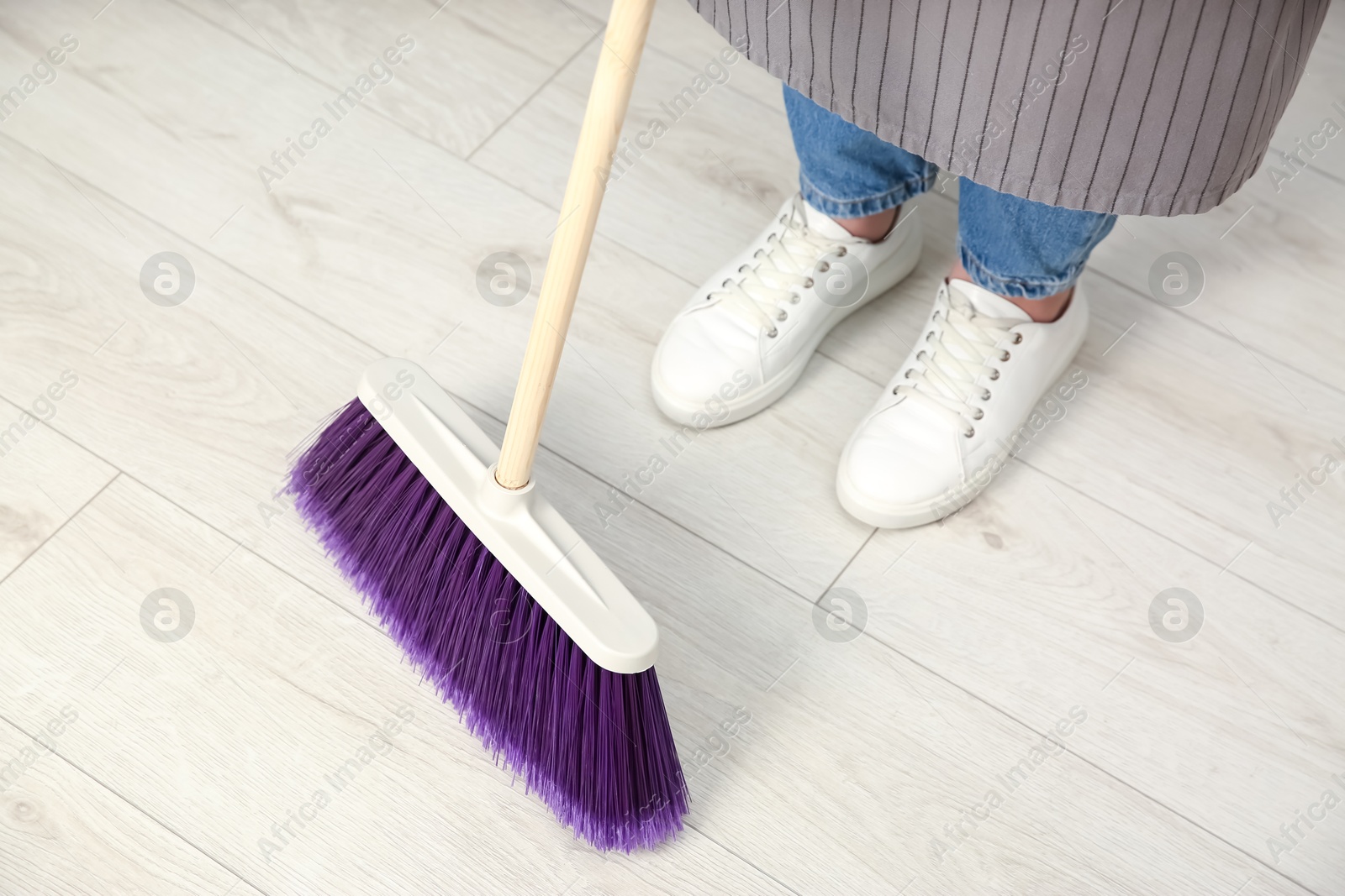 Photo of Woman with broom sweeping floor indoors, closeup