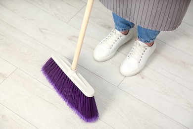 Photo of Woman with broom sweeping floor indoors, closeup