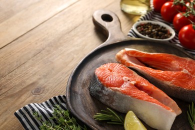 Photo of Board with fresh salmon steaks, lemon and rosemary on wooden table, closeup. Space for text