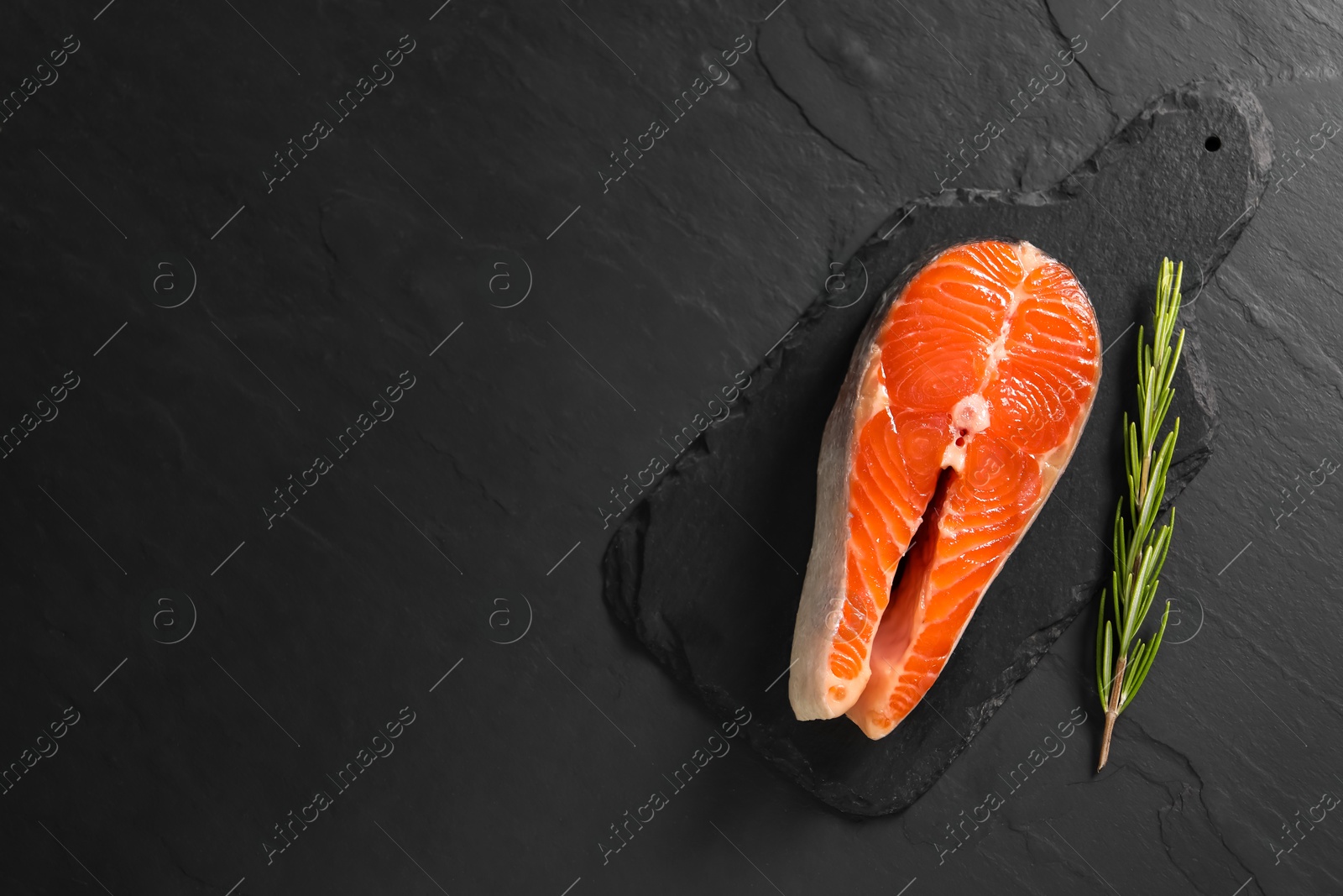 Photo of Fresh salmon steak and rosemary on dark textured table, top view. Space for text