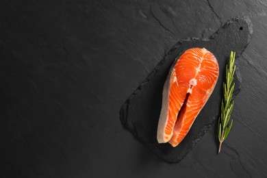 Photo of Fresh salmon steak and rosemary on dark textured table, top view. Space for text