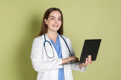 Professional nurse working with laptop on pale green background