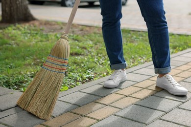 Photo of Woman with corn straw broom sweeping pavement outdoors, closeup