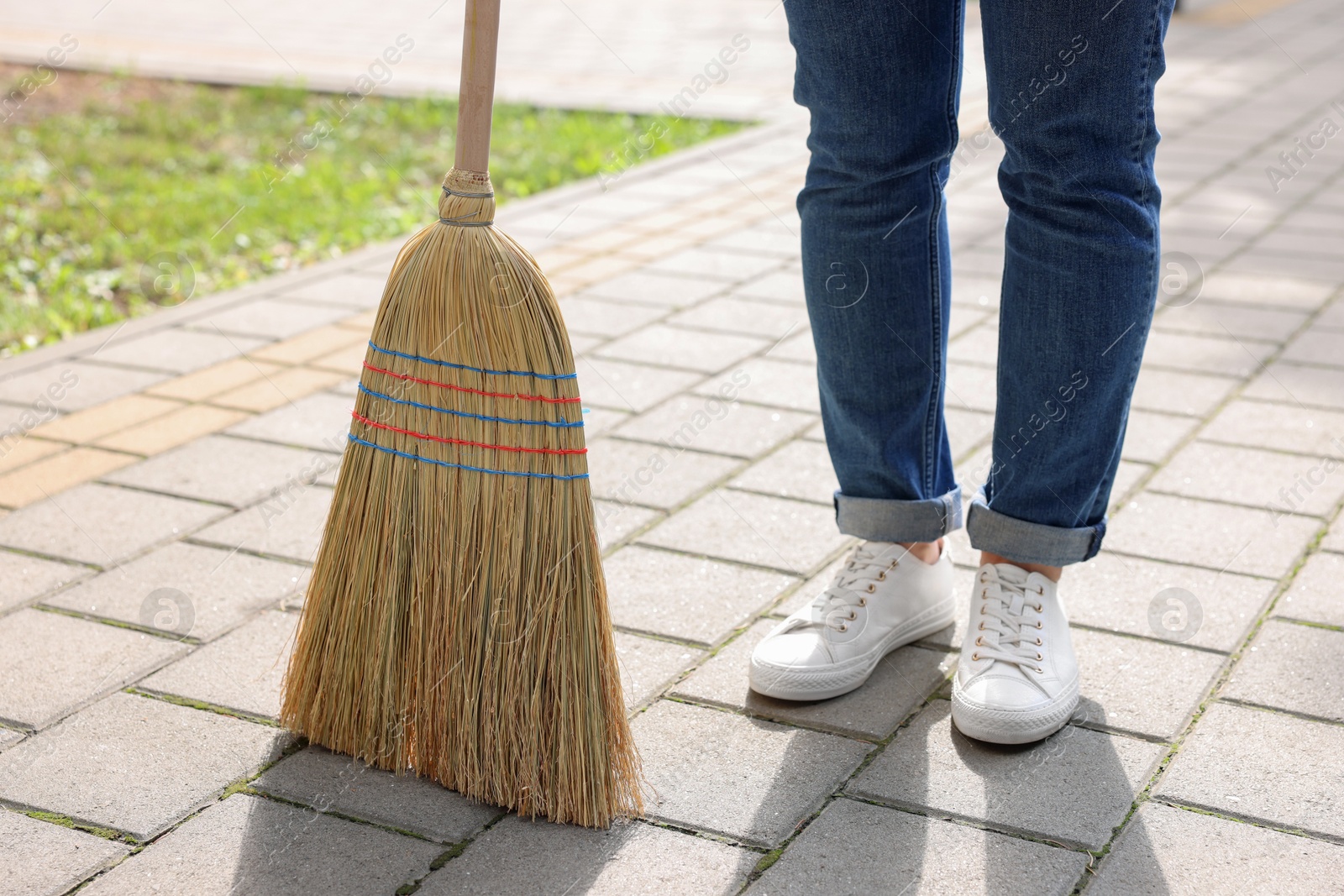 Photo of Woman with corn straw broom sweeping pavement outdoors, closeup