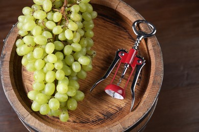 Photo of Wing corkscrew, grapes and wooden barrel on table, above view