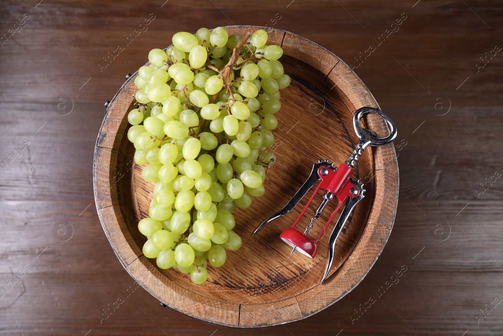 Photo of Wing corkscrew, grapes and wooden barrel on table, top view