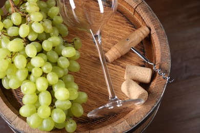 Corkscrew, glass, corks, grapes and wooden barrel on table, closeup