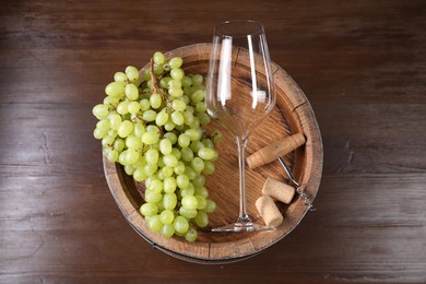 Photo of Corkscrew, glass, corks, grapes and wooden barrel on table, top view