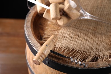 Corkscrew, corks, glass and wooden barrel on table, closeup