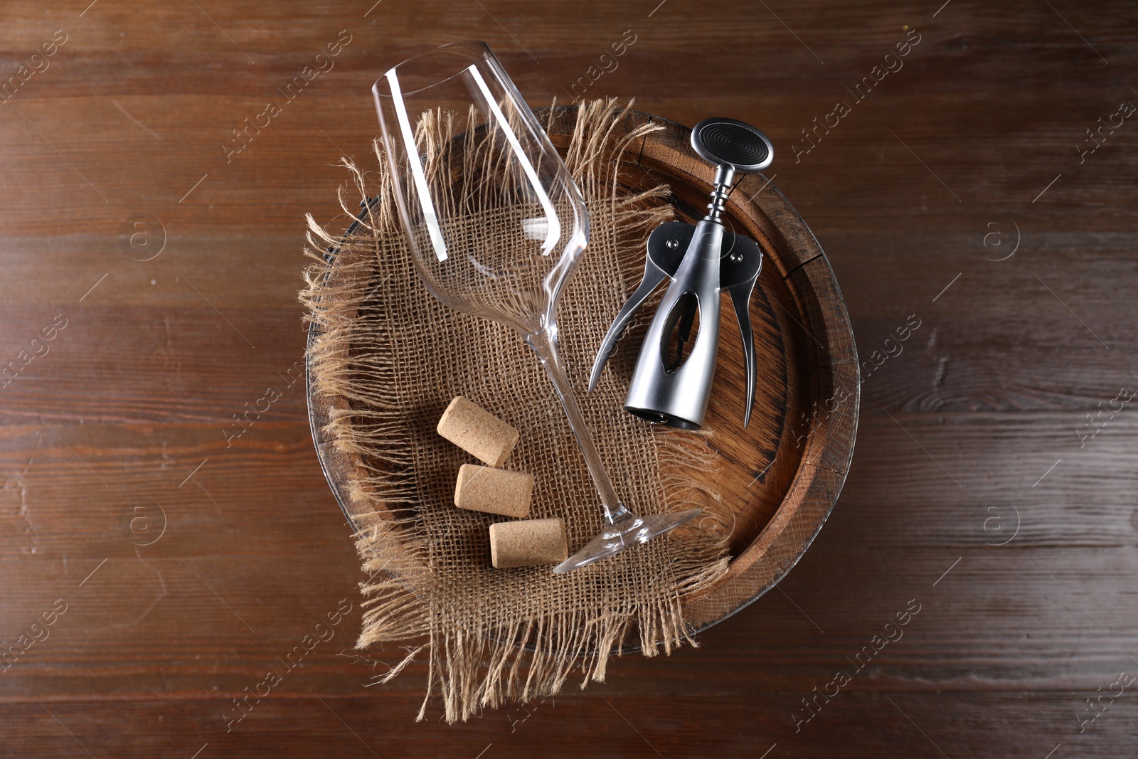 Photo of Wing corkscrew, corks, glass and wooden barrel on table, top view