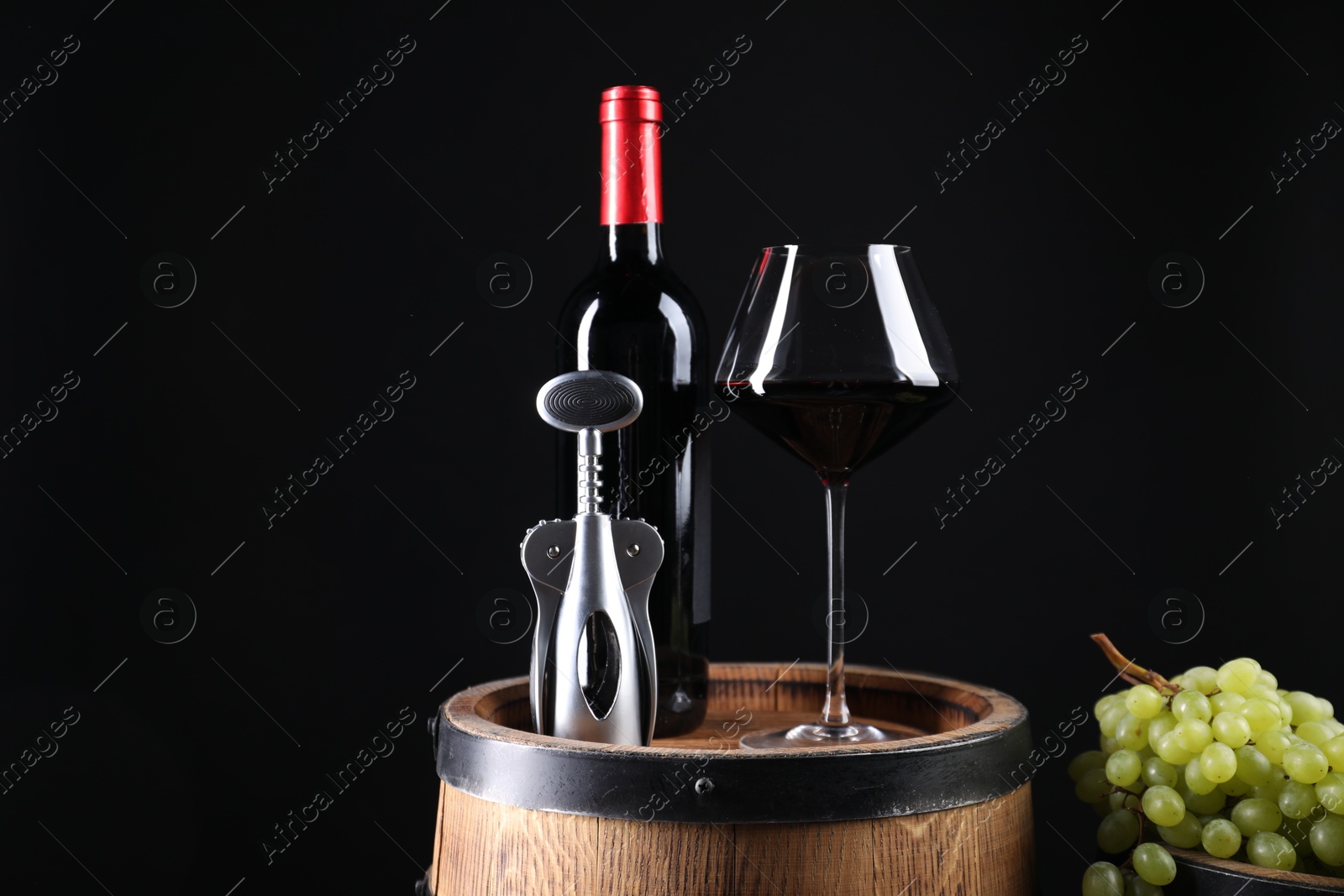 Photo of Wing corkscrew, bottle of wine, glass, grapes and wooden barrel against black background