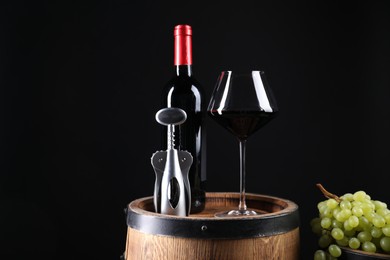 Photo of Wing corkscrew, bottle of wine, glass, grapes and wooden barrel against black background