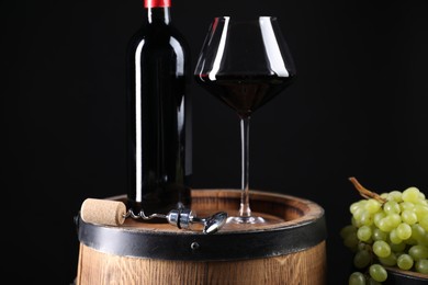 Corkscrew with metal handle, bottle of wine, glass, grapes and wooden barrel against black background