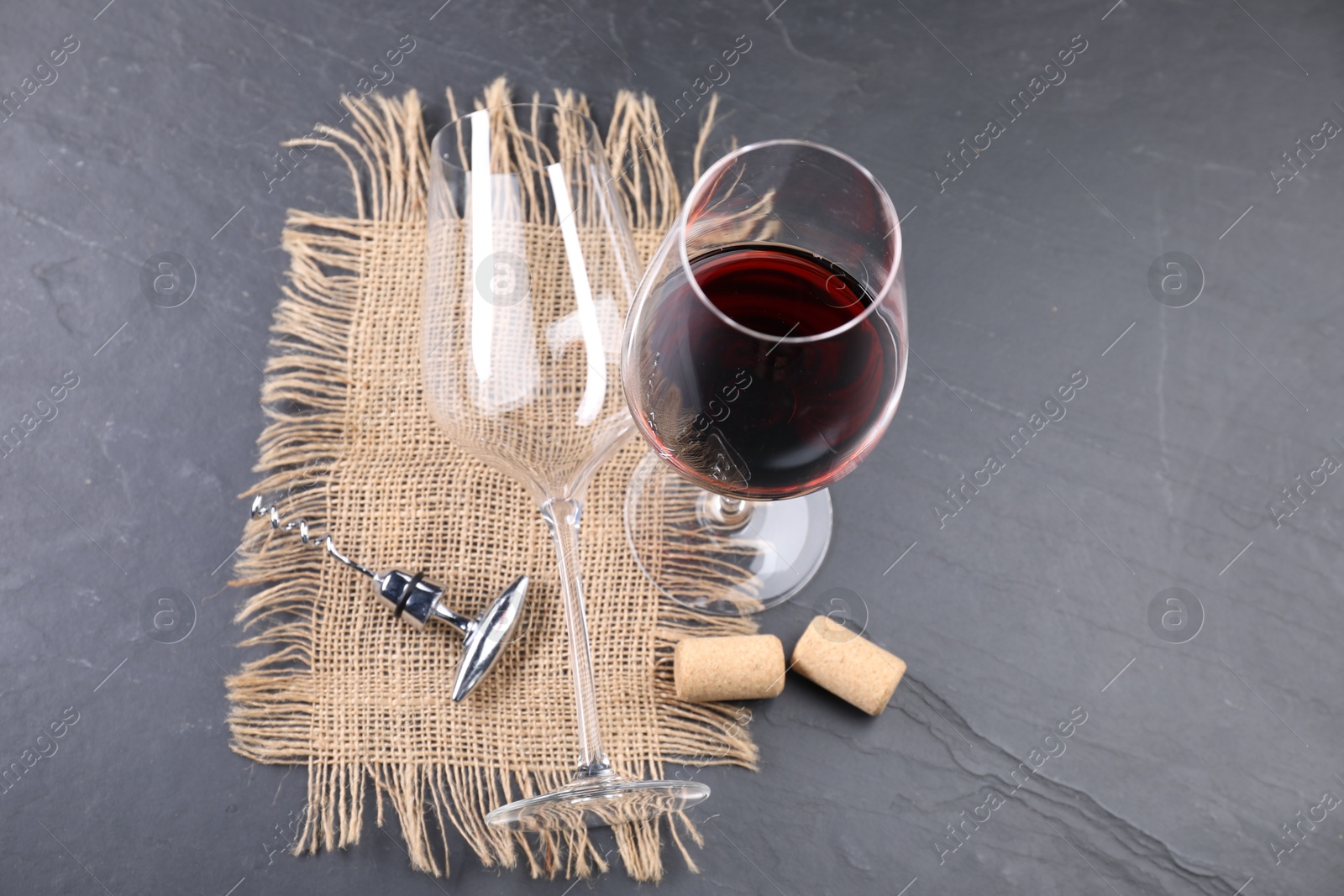 Photo of Corkscrew with metal handle, corks and glass of wine on grey table