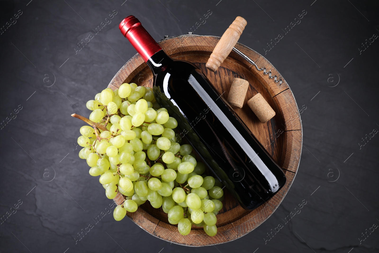 Photo of Corkscrew, bottle of wine, grapes, corks and wooden barrel on grey table, top view