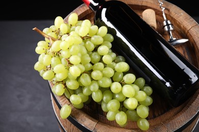 Corkscrew with metal handle, bottle of wine, grapes, cork and wooden barrel on grey table, closeup