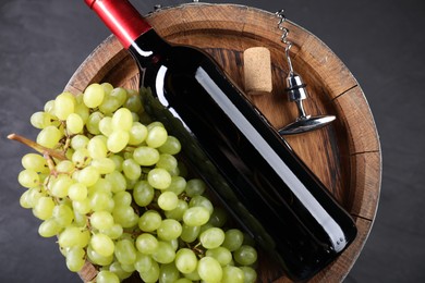 Photo of Corkscrew with metal handle, bottle of wine, grapes, cork and wooden barrel on grey table, top view