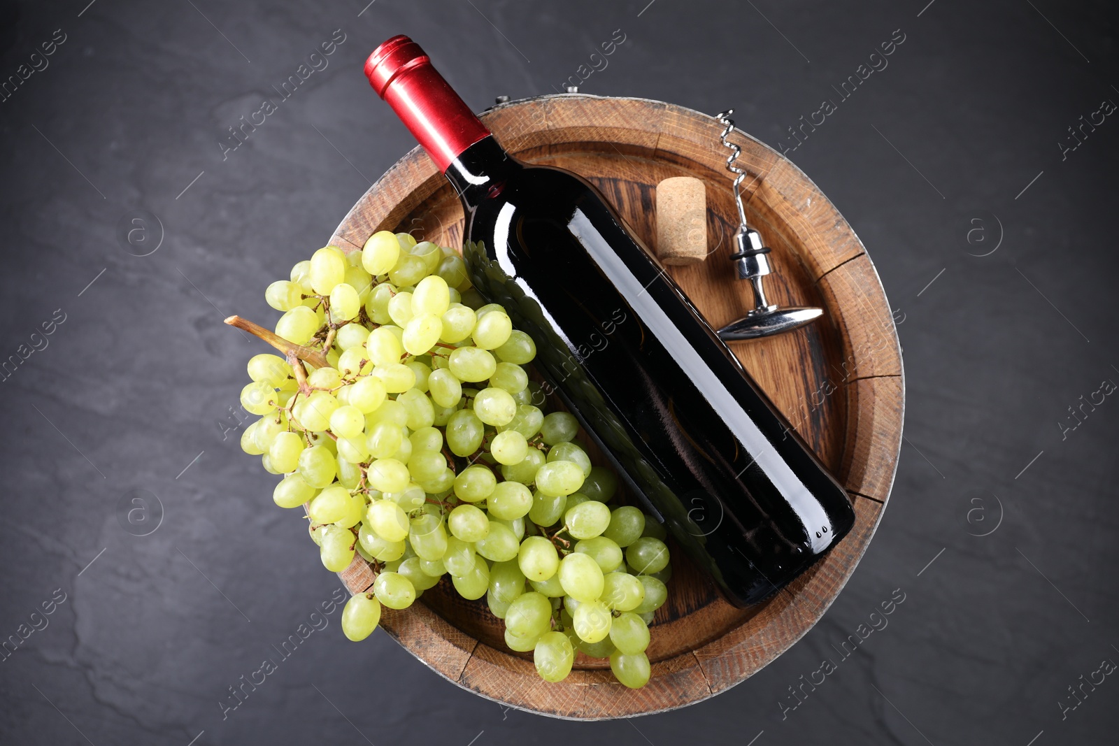 Photo of Corkscrew with metal handle, bottle of wine, grapes, cork and wooden barrel on grey table, top view