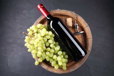 Corkscrew with metal handle, bottle of wine, grapes, cork and wooden barrel on grey table, top view