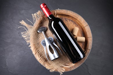 Photo of Wing corkscrew, bottle of wine, corks and wooden barrel on grey table, top view